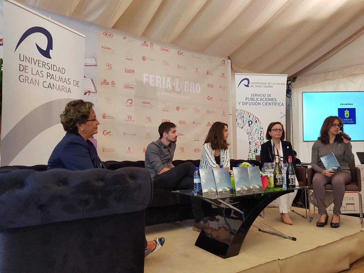 Vista parcial de la carpa en la que un grupo de personas, sentadas en sofás, realiza la presentación. En primer plano, la directora de la Biblioteca Universitaria.