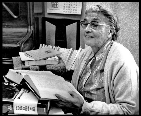 María Moliner Fotografía de María Moliner, sentada a una mesa, entre libros, hojeando uno de los tomos de su diccionario.