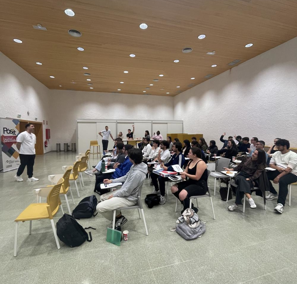 Salón de actos diáfano con decenas de personas sentadas mientras un hombre da una charla de pie