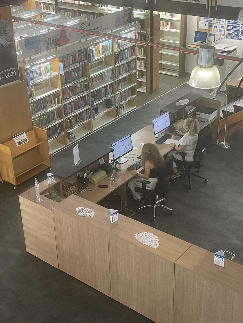 Vista desde piso superior del área de recepción y mostrador de préstamo de una biblioteca con personal.