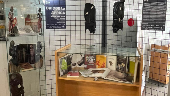 Expositor de cristal con libros de temática africana, junto a máscaras africanas y carteles del evento Bridge to Africa.