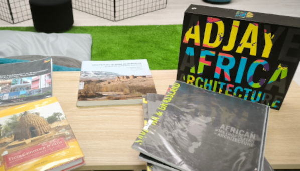 Mesa con exposición de libros de arquitectura africana, destacando una caja con el texto David Adjaye