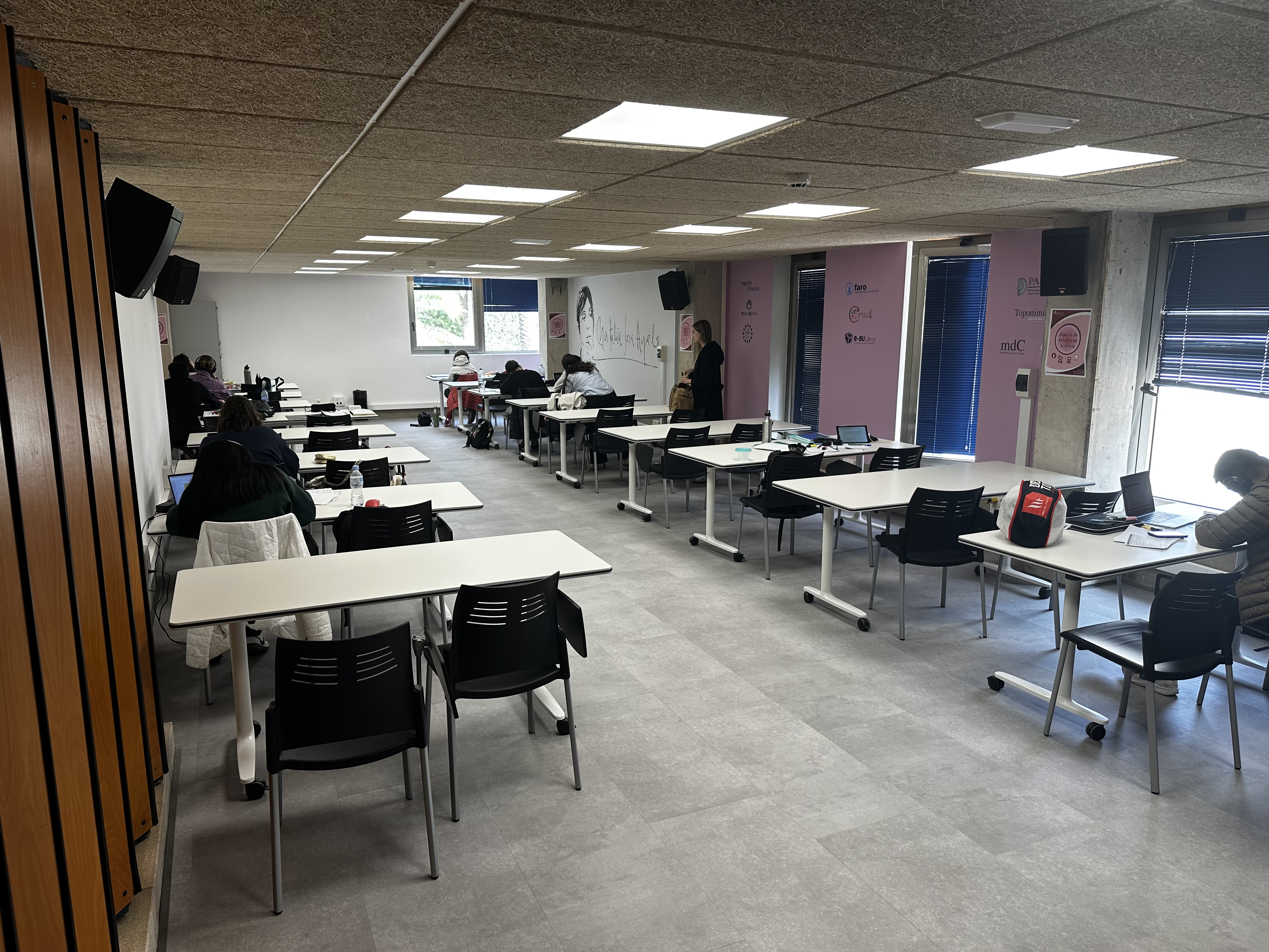 Sala con mesas de estudio y estudiantes.