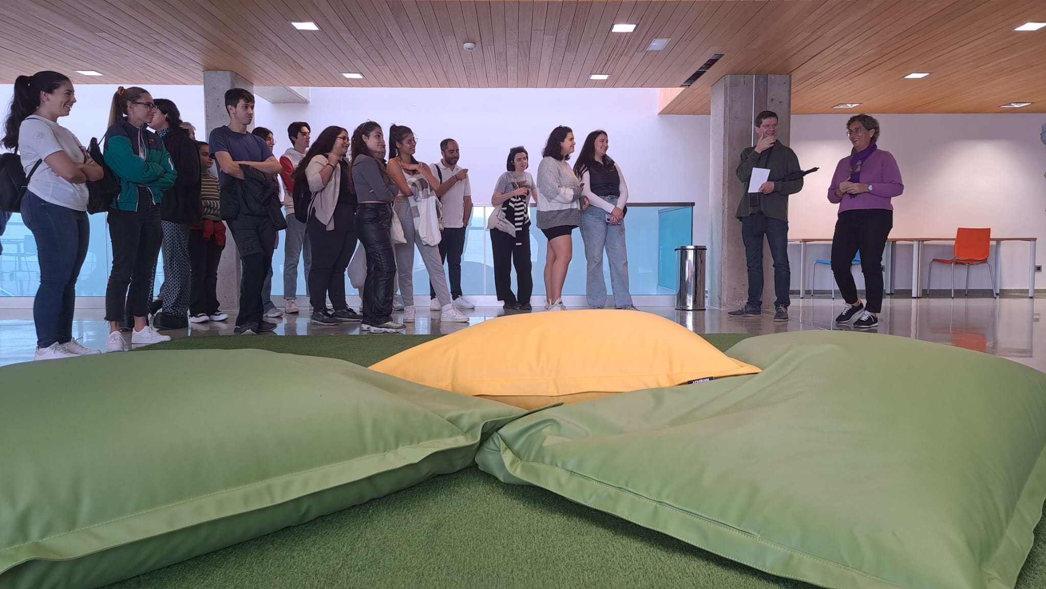 Vista de grupo de personas visitando sala de biblioteca con alfombra y cojines, mobiliario moderno y espacios diáfanos