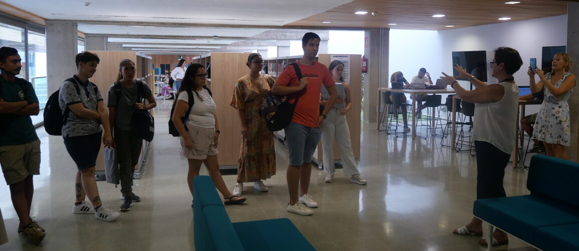 Un grupo de estudiantes atiende indicaciones de una bibliotecaria en una sala de biblioteca