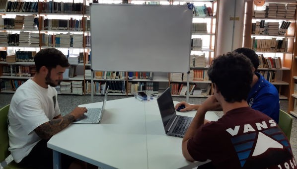 Mesa 4 Tres alumnos estudian con ordenadores portátiles en una mesa de una biblioteca.